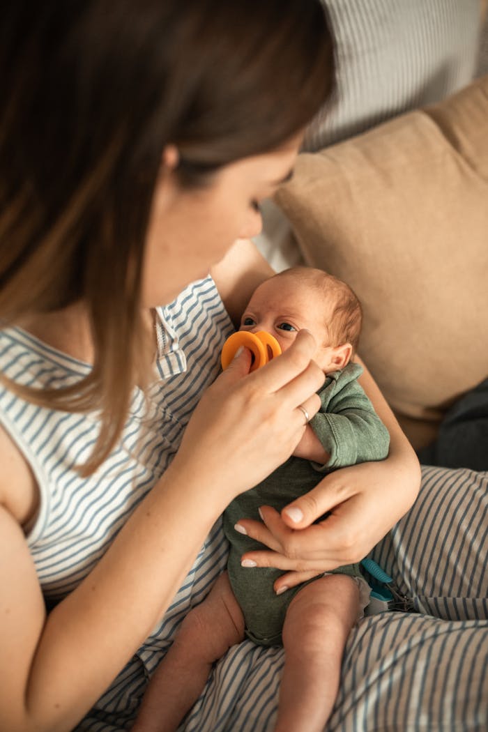 Crafting Captivating Headlines: Your awesome post title goes here A mother tenderly feeds her newborn baby with a bright orange pacifier indoors.